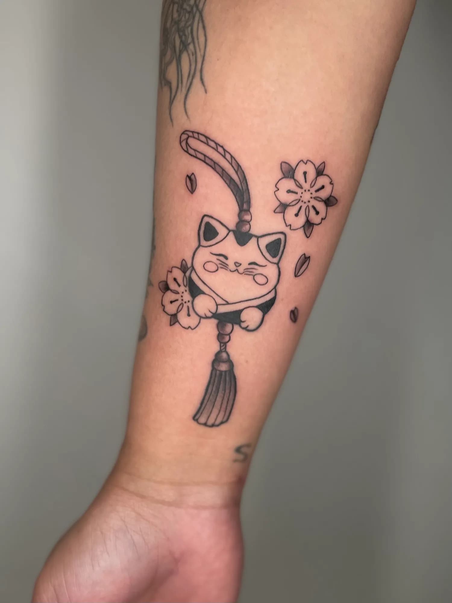 Small black and grey cat charm forearm tattoo by Kamy Cao.